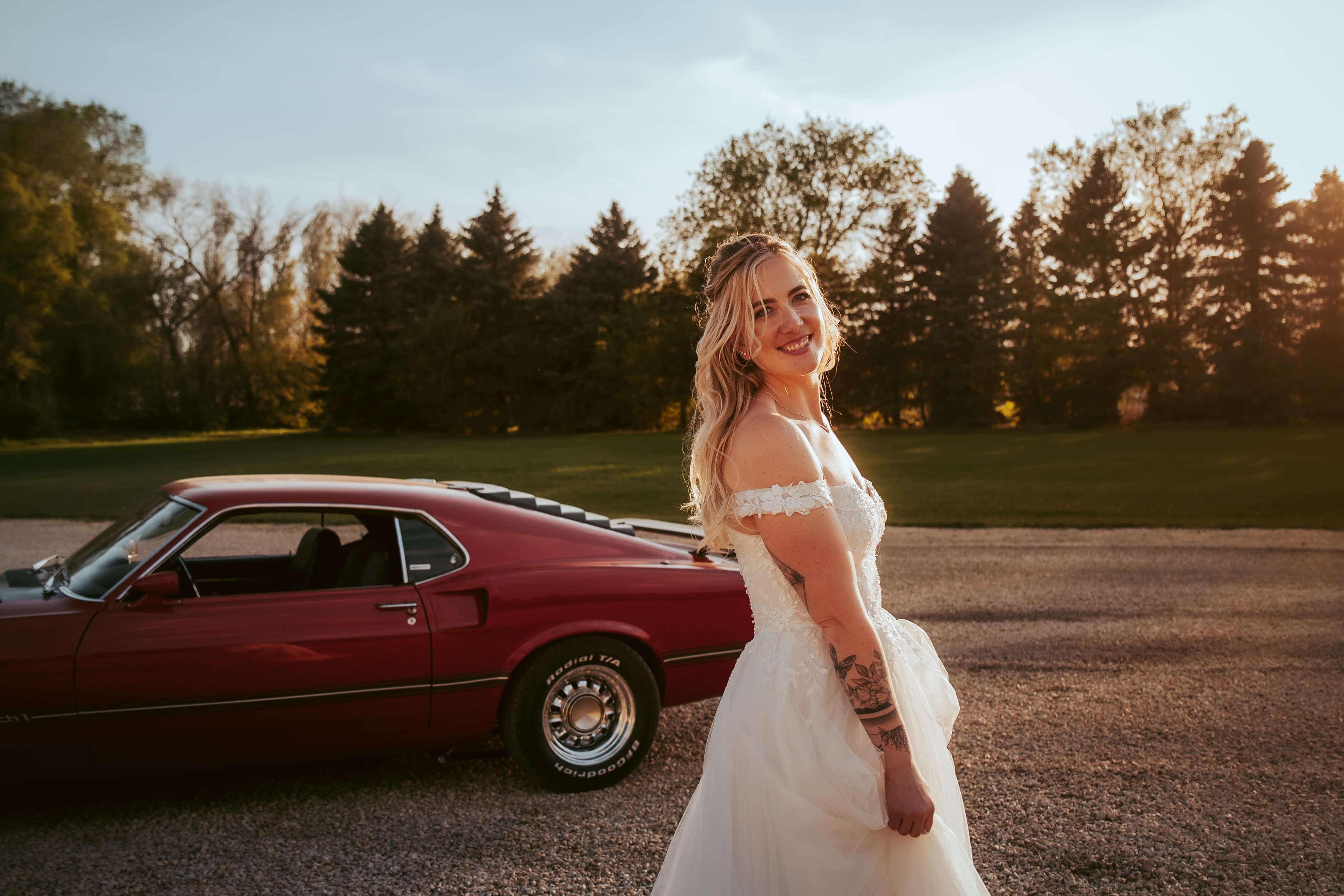 Bride standing infront of a red classic ford mustang.