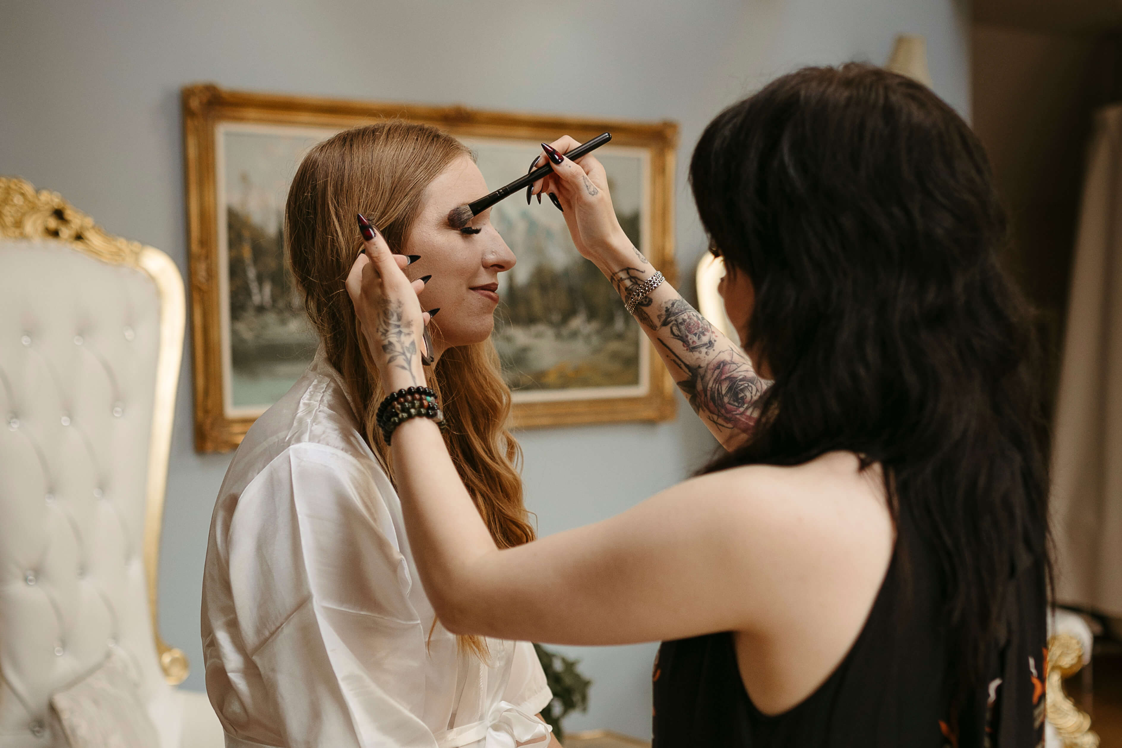 Makeup artist applies makeup to the bride dressed in a white rob.
